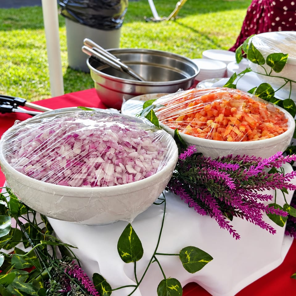 Covered bowls of chopped garnishes on a red buffet table decorated with greenery