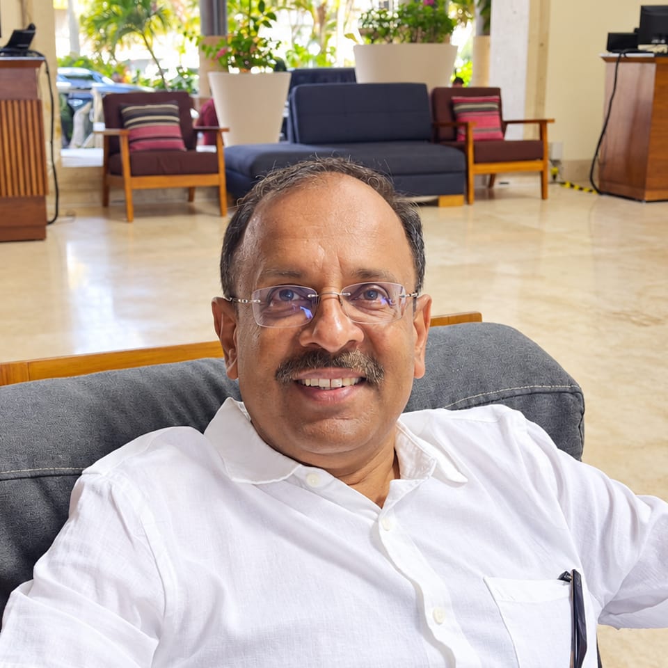 Guest in glasses seated in a hotel lounge with reception desk and seating behind him