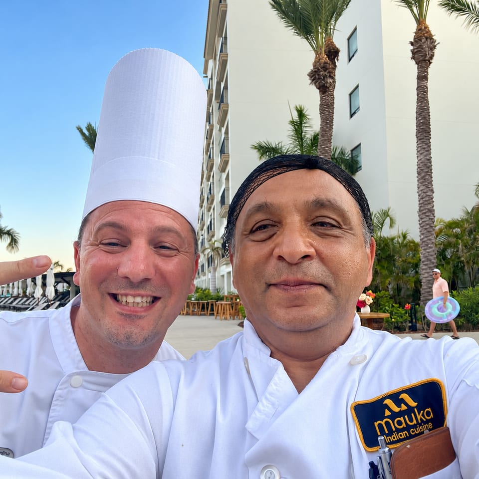 Two chefs posing outdoors beside palm trees