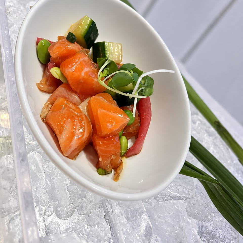 Orange-colored bites with cucumber and greens in a white serving bowl