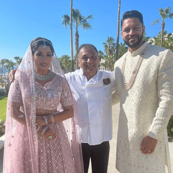 A chef with a Mauka Indian Cuisine logo stands with a bride and groom in traditional Indian attire.