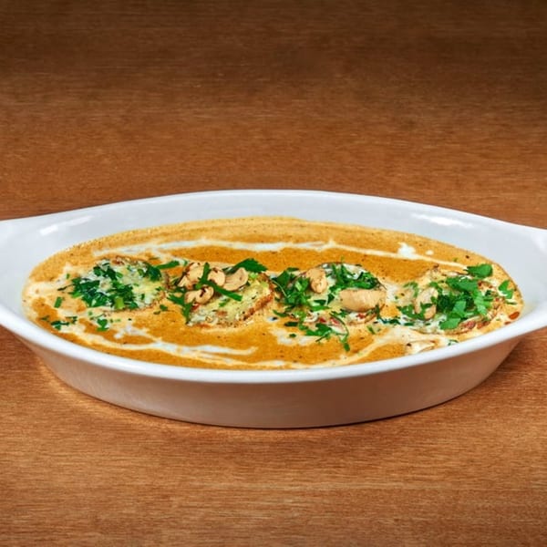 Indian dish with creamy orange sauce, topped with green herbs and cashews, in a white oval dish.