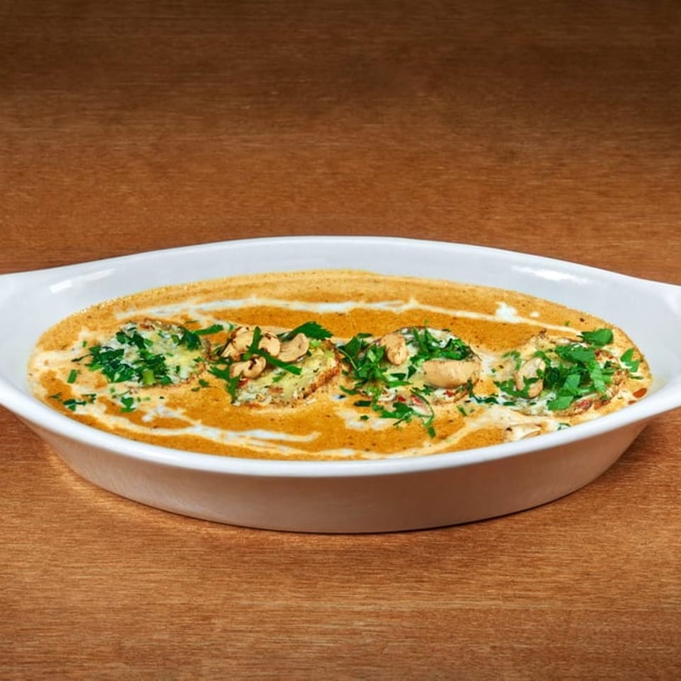 Indian dish with creamy orange sauce, topped with green herbs and cashews, in a white oval dish.