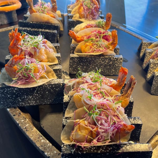 Rows of shrimp tacos with red cabbage and microgreens on speckled black holders.