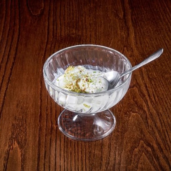 Kulfi, an Indian frozen dessert, in a glass bowl with a spoon, topped with pistachios.