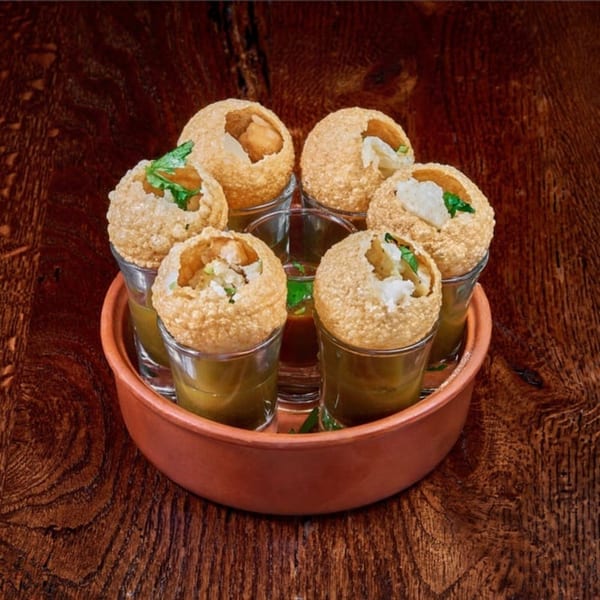 Six pani puri, filled with potato and herbs, served in shot glasses with dipping sauce.