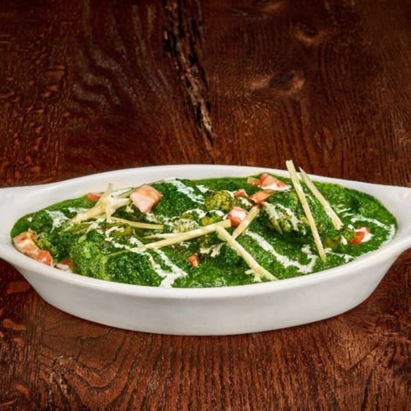 Mauka Indian Cuisine's vibrant green Palak Paneer, garnished with cream, ginger, and paneer, in a white dish.