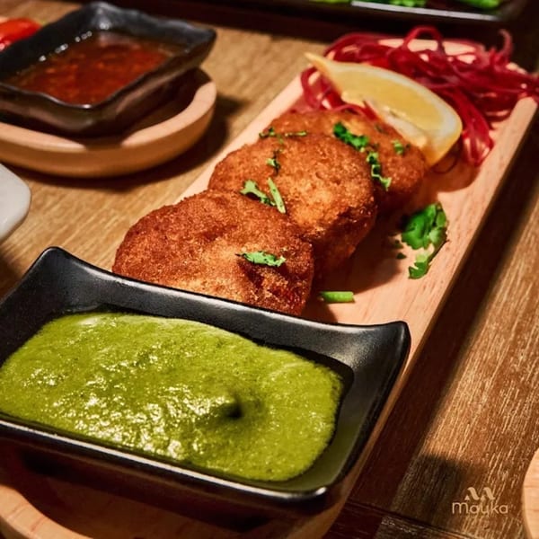 Golden-brown Indian cutlets with green chutney, red onions, and a lemon wedge on a wooden board.