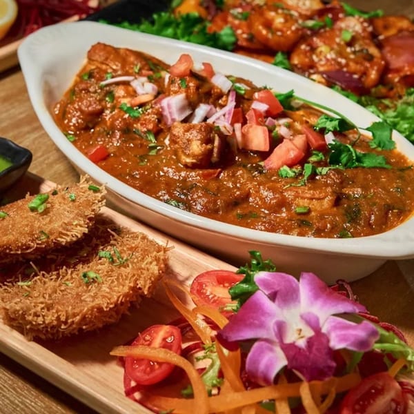 A white dish of Indian curry with diced tomatoes and onions, alongside crispy fried appetizers.