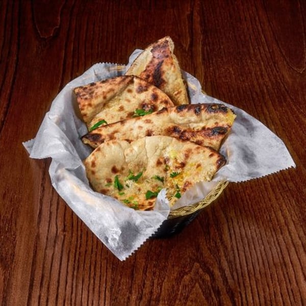 A basket of golden-brown Indian naan bread, garnished with fresh green herbs, on a wooden table.