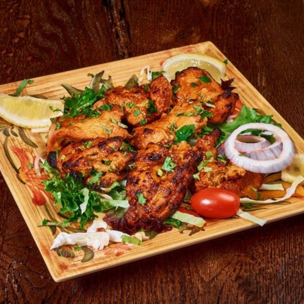Indian chicken tikka with lemon, onion, and tomato on a decorative plate.
