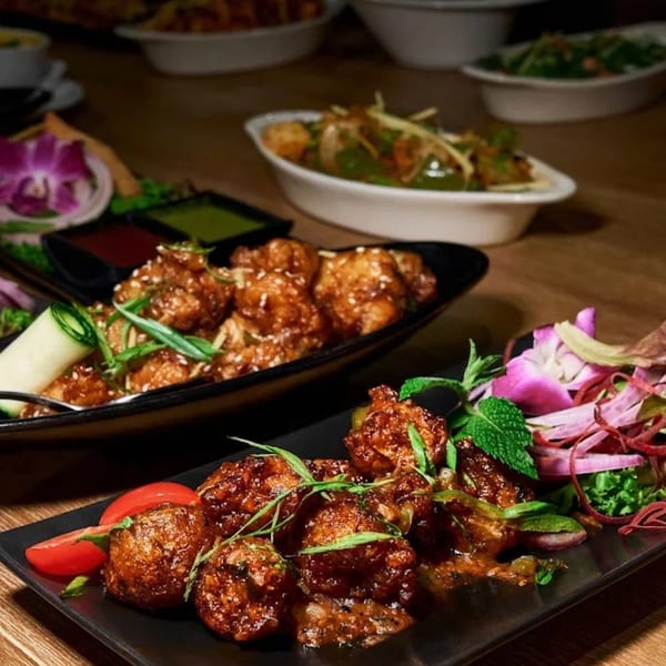 Close-up of Indian appetizers, including Manchurian and chili paneer, on a dark wooden table.