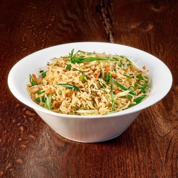 A white bowl filled with Indian fried rice, garnished with green onions and vegetables, on a wooden table.